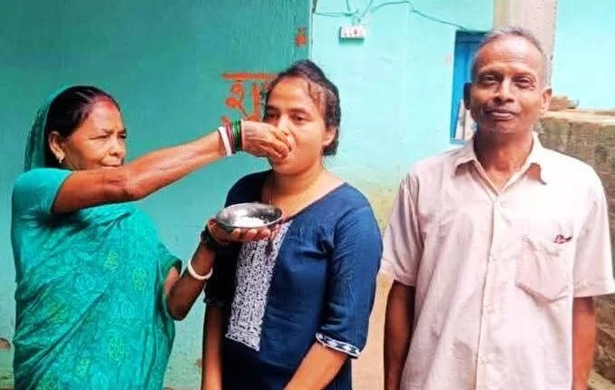 चीनी खिलाकर बेटी का मुंह मीठा कराती मां, साथ में हैं पिता।